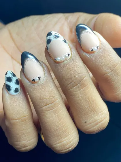A playful French manicure with black tips, pearl details, and a cow print accent nail.