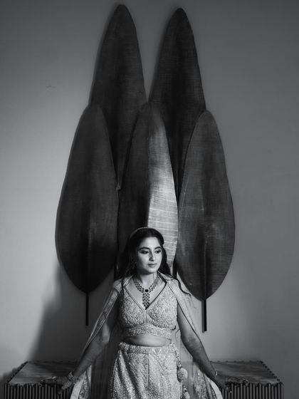 A graceful black and white portrait of the bride in her reception lehenga, showcasing her elegance against a modern, artistic backdrop.
