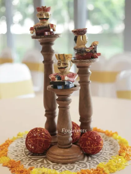 A close up of a unique table centerpiece inspired by Rajasthani culture. The decor features hand painted wooden figurines of traditional musicians placed on tiered wooden stands, surrounded by marigold petals.