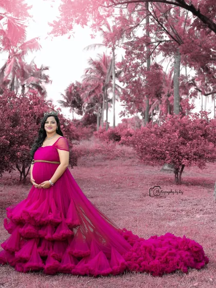 A stunning outdoor portrait with a pink theme. The mother-to-be wears a ruffled gown and crown, surrounded by pink-toned foliage.
