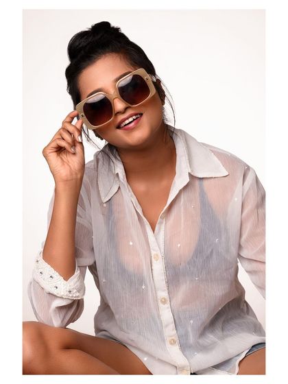 A casual and fun studio portrait. The oversized sunglasses and sheer shirt create a relaxed, summery feel, ideal for a lifestyle or accessory brand shoot.