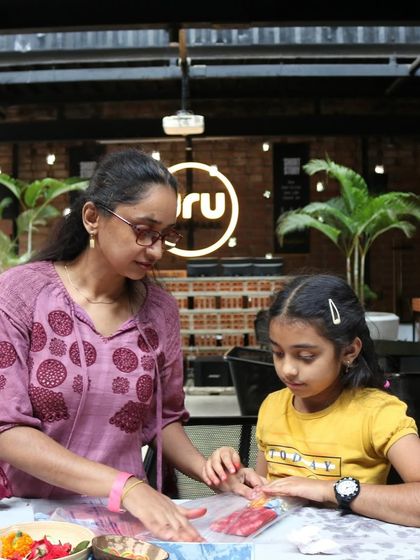 A mother and daughter work side-by-side on a flower pounding craft in an indoor workshop setting. This shows how our activities can be adapted for different locations, always focusing on the parent-child connection.