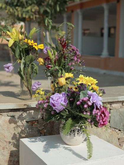 A close-up of a floral centerpiece from the lavender and yellow Haldi, featuring a mix of sunflowers, purple roses, and other wildflowers in a simple vase.