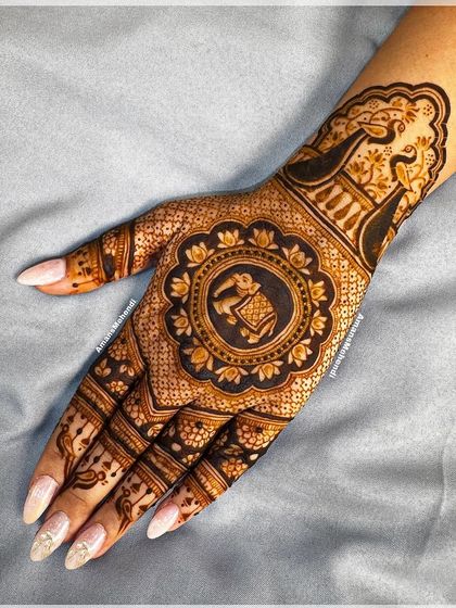 An elegant back-of-hand design with a central mandala featuring a royal elephant. The wrist is adorned with a peacock, creating a beautiful and balanced composition.