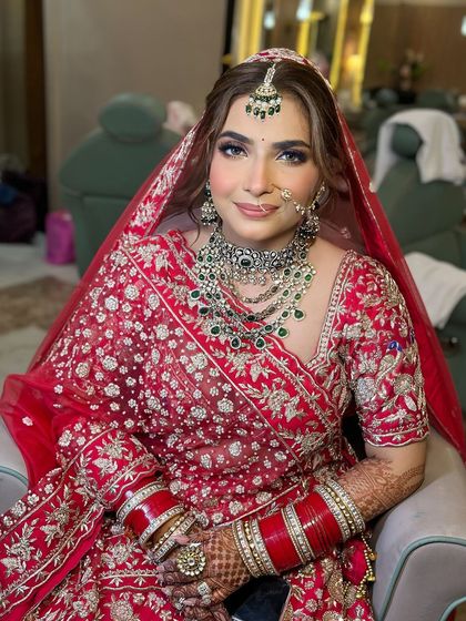 A radiant bride ready for her celebrity-style wedding. The look features a flawless base, subtly smoked-out eyes, and a soft lip, allowing her magnificent green and white kundan jewellery to stand out against the red outfit.