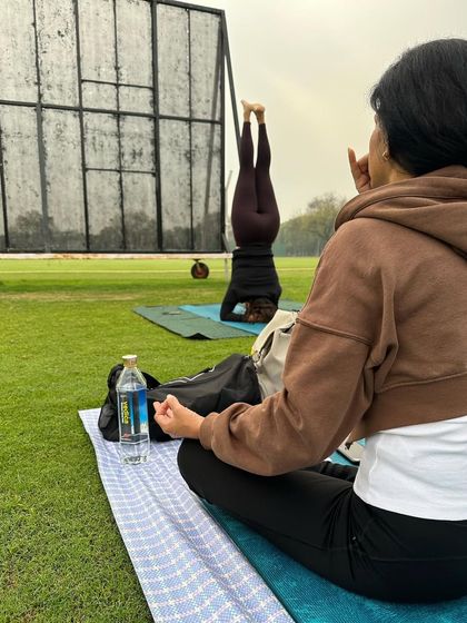 Regular practice makes good health. A student meditates while another practices headstand in the park.
