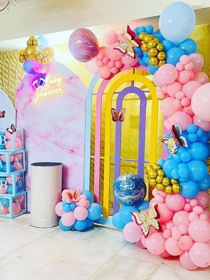A vibrant and modern baby shower setup with a butterfly theme. This design uses multiple arched backdrops with a marble pattern, colorful balloon garlands, and 'BABY' blocks for a multi-dimensional photo opportunity.
