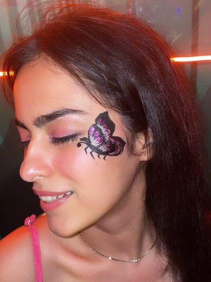 A detailed butterfly glitter tattoo with purple and black accents. I use stencils to create intricate and beautiful designs like this.