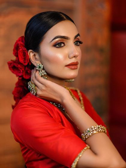A close-up portrait focusing on the model's expressive look and the vibrant red of her outfit and the roses in her hair. The lighting is soft and flattering, ideal for beauty-focused traditional shots.