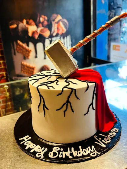 A Thor-themed cake worthy of a superhero, featuring Mjolnir smashing into the top and a fondant cape draping down the side.