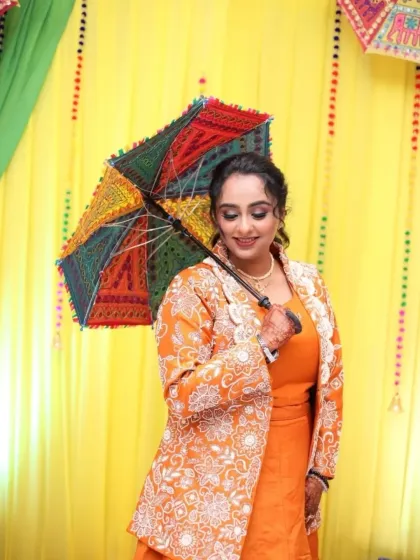 A vibrant Mayera look. The bride's bright orange outfit is paired with a colorful umbrella prop, and her makeup is kept fresh and defined to match the festive atmosphere.