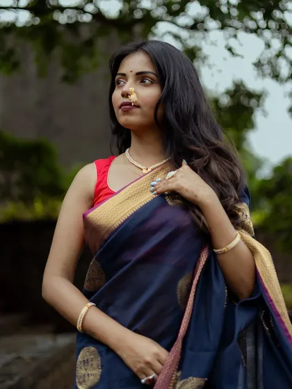A classic three-quarter portrait. The model, wearing a traditional blue saree and a simple pearl necklace, looks away from the camera, creating a timeless and elegant feel against a soft, natural background.
