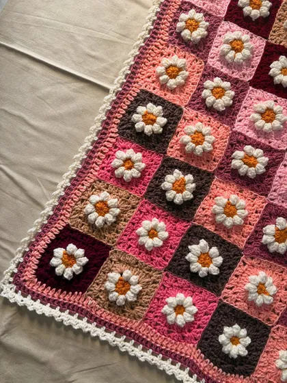 A close up corner view of the Daisy blanket, highlighting the texture of the 3D flower petals and the detailed stitch work of the border. We use soft, high quality acrylic yarn that is gentle on a baby's skin.