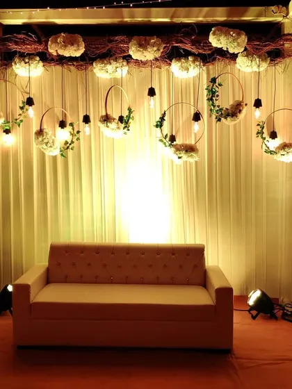 A rustic photo backdrop featuring a white curtain, hanging floral hoops with Edison bulbs, and a frame made of natural branches. This design is both simple and incredibly photogenic.