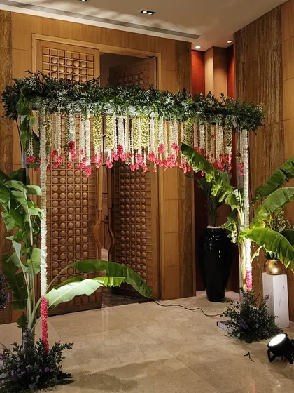 A lush entrance arch for an indoor ceremony, using banana plants and hanging floral strings to create a tropical and traditional feel.