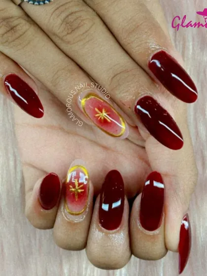 Deep, glossy red nails are paired with a stunning accent nail featuring a golden starburst on a red-to-nude ombré base. This look is the perfect combination of classic elegance and modern art.