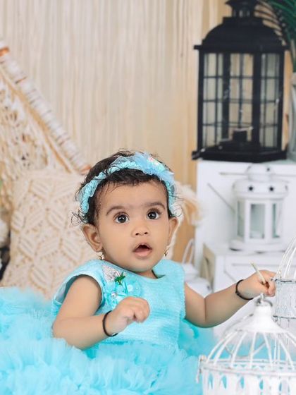 A baby girl in a light blue dress explores the decorative birdcages in a whimsical boho setup. Her curious expression adds a touch of wonder to the scene.