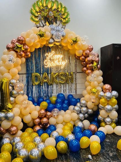 This birthday ring decoration features a "Happy Birthday" neon sign as the centerpiece. The sign glows brightly against the blue foil curtain and balloon arch.