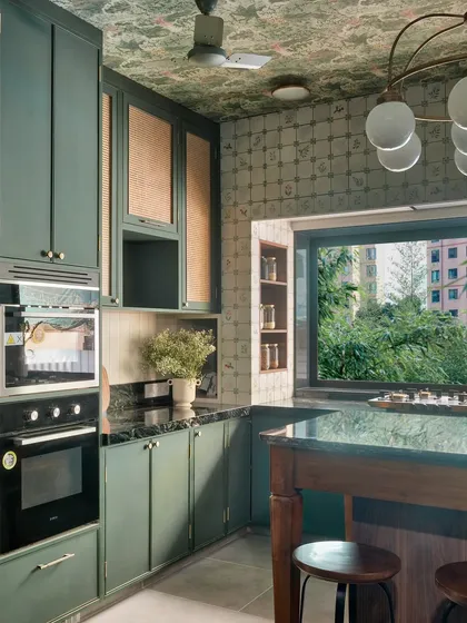Another perspective of the green kitchen, showing the relationship between the island, the main counter, and the large window. The layout is designed for easy movement and social interaction.