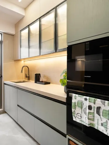 This kitchen features an integrated oven and fluted glass upper cabinets, which add texture while partially obscuring the contents. The warm under-cabinet lighting highlights the clean lines and matte finish of the lower cabinets.