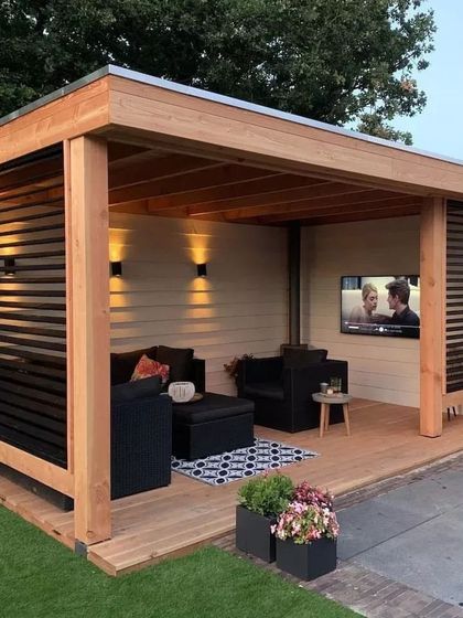 A modern, freestanding pergola designed as an all-weather outdoor media room. It features comfortable lounge seating, integrated lighting, and a wall-mounted television, completely redefining the concept of a backyard hangout.