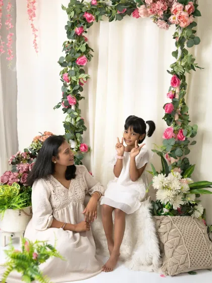 A mother looks on lovingly as her daughter makes a peace sign for the camera, a cute and candid moment.