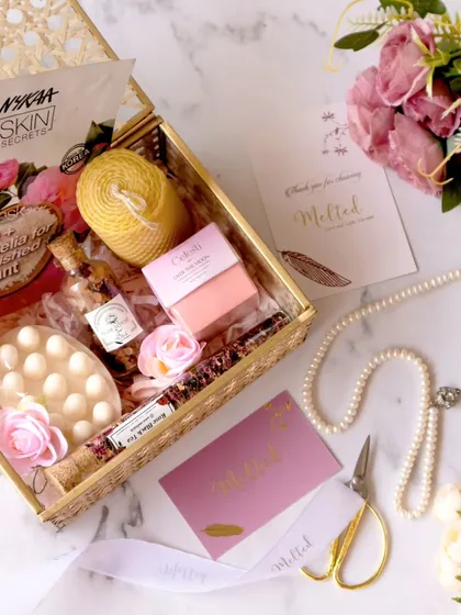 An overhead shot of a curated gift box, complete with a Nykaa skin secrets mask, pearls, and floral elements. The composition is a beautiful blend of textures and soft colors, creating a luxurious feel.