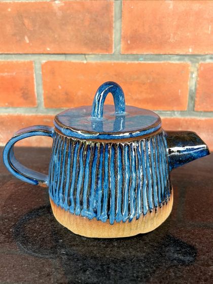 A beautiful hand-built teapot with a carved vertical line texture and a deep blue glaze. This piece was made by a student and shows incredible attention to detail.