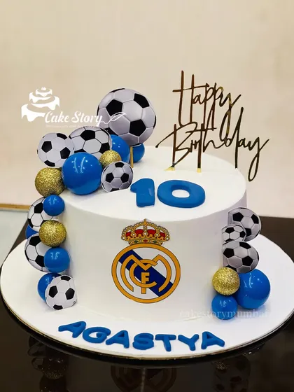 A football-themed cake for a 10th birthday. This design features the Real Madrid logo and is decorated with a cascade of edible footballs and blue and gold spheres.