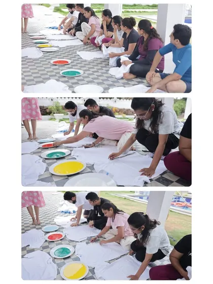 Participants are seated on the floor, beginning to apply paint to their t-shirts after a guided meditation. The setup is communal and grounded, encouraging a sense of shared experience and mutual support.