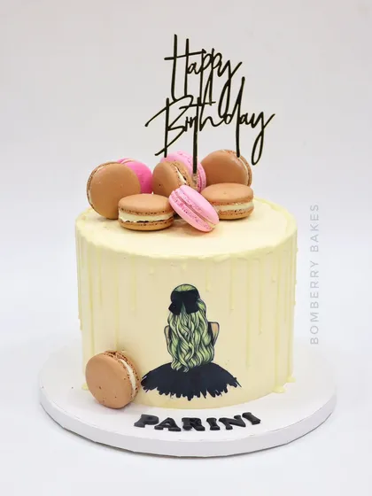 A chic birthday cake with a hand-painted girl silhouette, topped with delicious vegan macarons.
