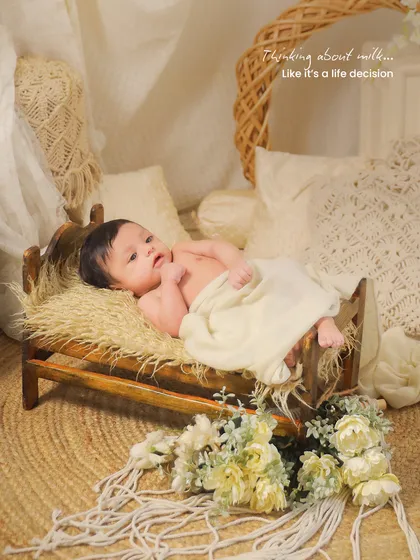 A newborn lies awake in a miniature wooden bed, part of a rustic, bohemian-themed set. This captures a quiet, thoughtful moment.