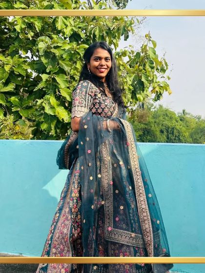 A client looking lovely against a bright blue wall in a dark teal floral lehenga. The colors pop beautifully.