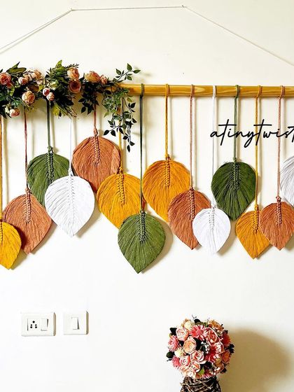 Celebrating a milestone of 100 leaf wall hangings sold! This version features a beautiful mix of earthy greens, yellows, and whites, adorned with artificial flowers.
