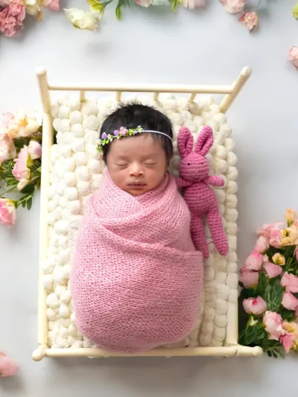 Sleeping soundly in a miniature bed, this newborn is surrounded by soft pink flowers. These styled setups create beautiful, dreamy portraits.