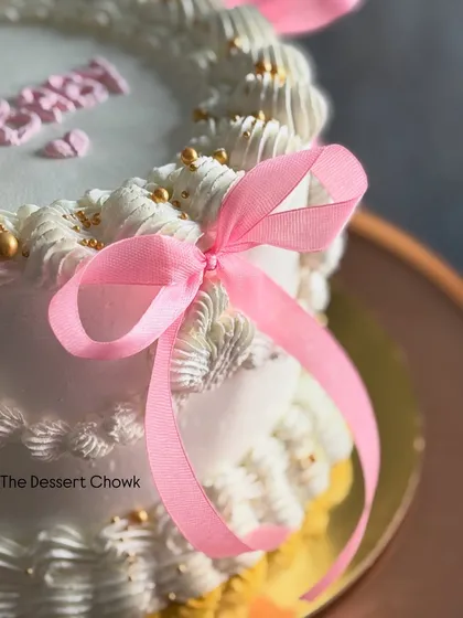 A close-up of the delicate pink ribbon tied on this white Lambeth-style cake.