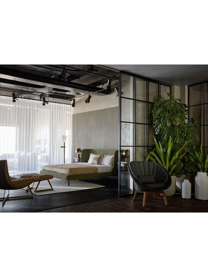 A bedroom vignette designed to feel like a modern, serene retreat. The space is defined by glass and metal partitions, with sheer curtains for privacy and a mix of indoor plants to create a connection to the outdoors.