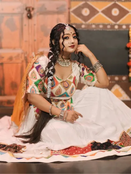 A full seated pose showcasing the entire 'Gori Radha' outfit, from the maang tikka to the detailed border of the skirt.