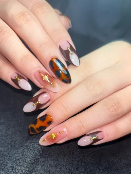 A sophisticated design combining a nude base, brown color blocks, and a tortoiseshell accent nail with gold star details.