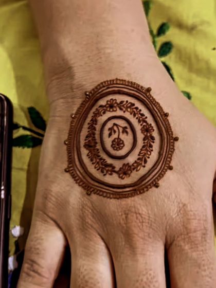 A unique and modern mandala design. The central motif is a simple flower stem enclosed within two circles, creating a clean and artistic look on the back of the hand.