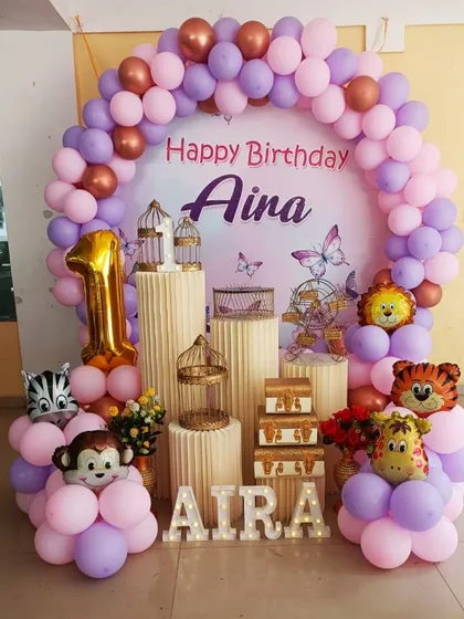 A cute and simple animal-themed setup for a first birthday. The decor uses a pastel balloon arch with adorable animal-shaped foil balloons and decorative bird cages.