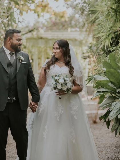 A couple walks hand-in-hand through one of the green pathways at Farmhouse Collective. The lush plants on either side create a beautiful, natural corridor.