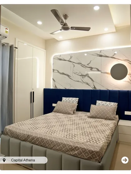 A bold and modern bedroom in Capital Athena. The deep blue upholstered headboard stands out against a white marble-finish wall with a unique circular light fixture.