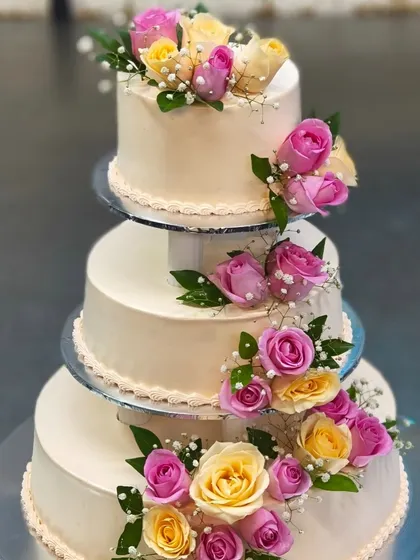 We believe your wedding cake should be as grand as your love story. This classic three-tiered cake, adorned with fresh pink and yellow roses, is a timeless centerpiece for any wedding celebration.