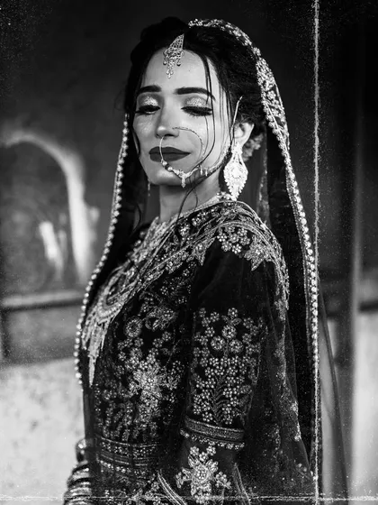 A serene and elegant black and white bridal portrait. The focus is on her calm expression and the beautiful details of her traditional wedding attire.