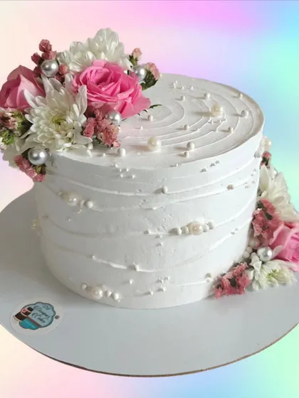 A white cake with a textured finish and decorated with fresh pink and white flowers. This design is simple, clean, and very elegant.