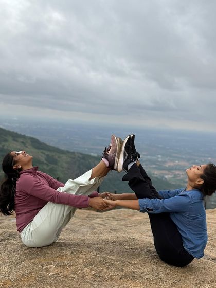 A partner boat pose on a mountain top. It's a playful way to build core strength while enjoying the beauty of nature and friendship.