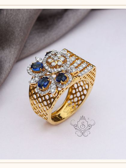 This is a custom cocktail ring that combines brilliant diamonds with deep blue sapphires in a floral arrangement. The intricate lattice work on the gold band adds another layer of artistry to this exquisite piece.