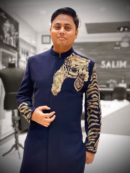 The designer wearing a custom navy blue Indo-Western jacket with a gold embroidered tiger on the shoulder and sleeve. This piece blends traditional silhouettes with fierce, modern artistry.