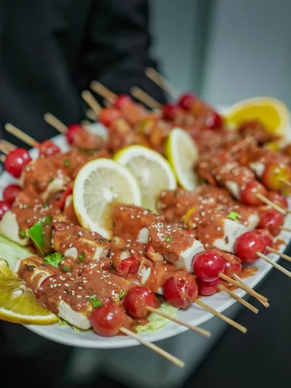A platter of chicken skewers ready to be served at a live event. Garnished with cherry tomatoes and lemon, these are as fresh and vibrant as they look.